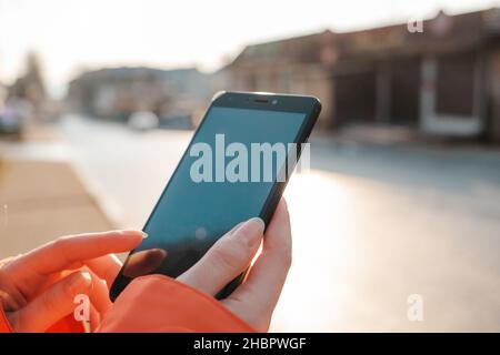 Il concetto di smartphone e Internet. Le mani delle donne stanno tenendo uno smartphone e capovolgendo qualcosa su di esso. Sullo sfondo, i negozi offuscati Foto Stock