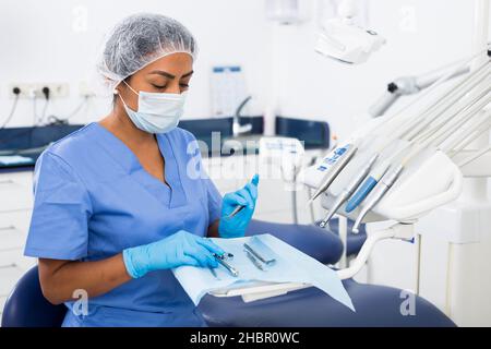 Dentista femminile focalizzato che si prepara a ricevere pazienti in studio dentistico, controllare e disporre gli strumenti Foto Stock