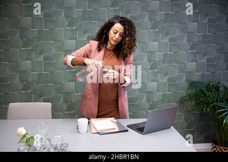 Donna d'affari incinta che versa l'acqua dalla bottiglia in vetro all'ufficio Foto Stock