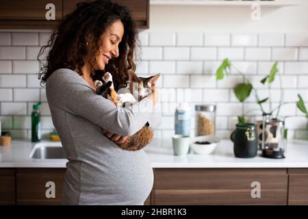 Donna incinta felice che porta il gatto in cucina Foto Stock