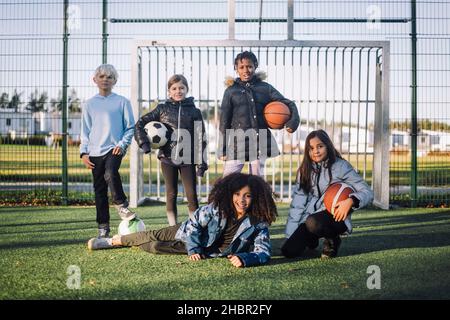 Ritratto di ragazze e ragazzo con palle sportive sul campo di calcio Foto Stock