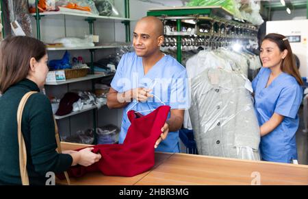 Smilante uomo drycleaner dando capi puliti al cliente, soddisfatti della qualità Foto Stock