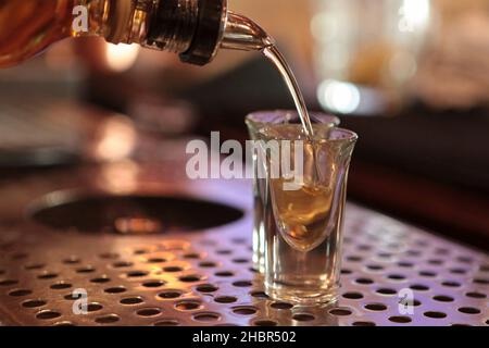Concetto di vita notturna versare alcol in due bicchieri da shot su un bancone bar Foto Stock