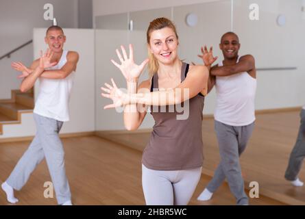 Ritratto di giovane donna allegra che pratica vigorosi movimenti di lindy hop in classe di danza di gruppo Foto Stock