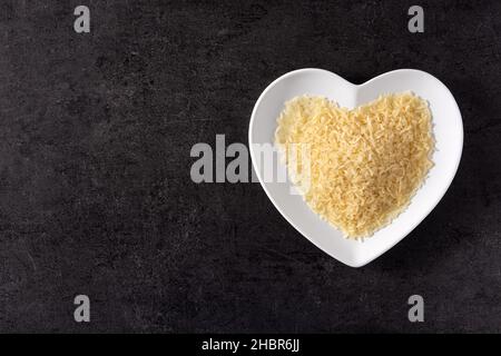 Riso crudo su piastra a forma di cuore su sfondo nero Foto Stock