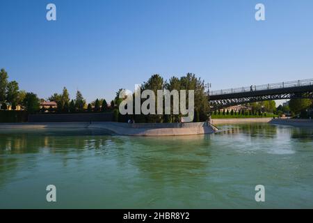 Un uomo si soleggia accanto al canale d'acqua dal fiume Chirchiq, accanto al Parco della repressione. A Tashkent, Uzbekistan. Foto Stock