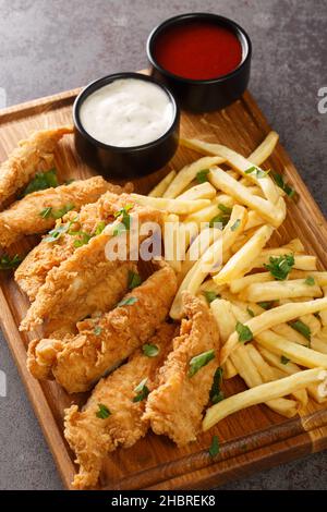 Strisce di pollo in fiocchi di mais breadcrumb servito con salsa di patatine fritte primo piano sul vassoio di legno verticale Foto Stock