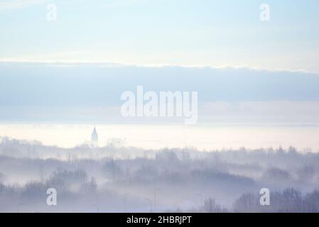 Profili di alberi e chiesa nella nebbia strisciando. Paesaggio invernale Foto Stock