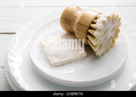 Sapone per piatti solido, ricoperto di schiuma. Stile di vita senza sprechi. Sapone per lavastoviglie su pelo di piatti con spazzola in sisal per la pulizia della cucina schiumosa. Foto Stock