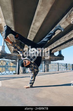 Il giovane uomo si rompe ballando su sfondo urbano con acrobazie acrobatiche. L'artista di strada frangidanze all'aperto Foto Stock