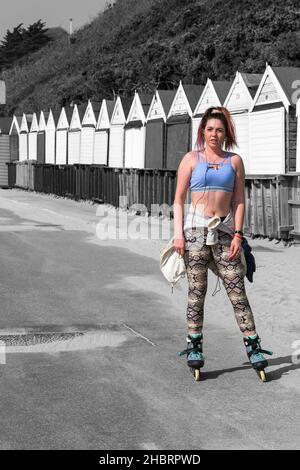 Giovane donna pattinatore a roller skater su roller skates roller blade sul lungomare da capanne da spiaggia a Bournemouth, Dorset Regno Unito nel mese di aprile Foto Stock