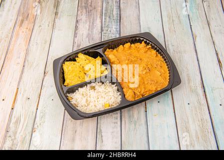 Stufato di pollo con salsa piccante di chipotle, riso bianco e nachos in un recipiente nero su tavola di legno Foto Stock