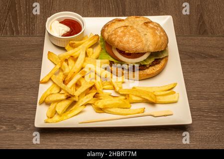Vista dall'alto di hamburger guarnito con patatine fritte, salse, cipolla bianca e pomodoro e pane del villaggio con bistecca di manzo Foto Stock