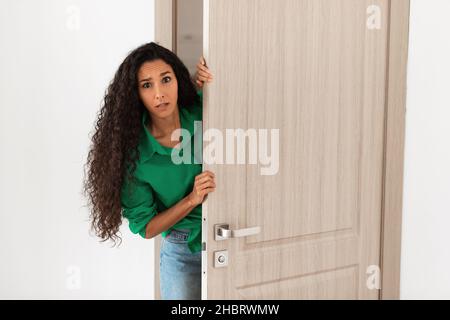 Signora confuso che guarda fuori dalla porta socchiusa Foto Stock