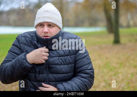 Giovane uomo freddo che indossa una borsetta di lana lavorata a maglia che si snuggling in giacca calda all'aperto in una fredda giornata autunnale Foto Stock