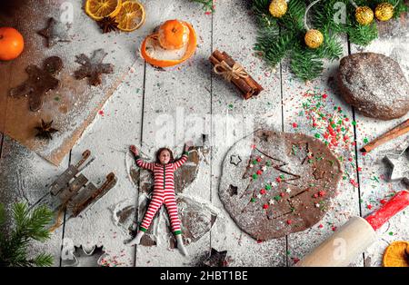 la bambina fa un angelo di neve sulla farina. cottura del pan di zenzero. Natale. Fotografia creativa Foto Stock