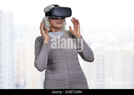 Sorpresa anziana donna caucasica indossando occhiali di realtà virtuale su sfondo sfocato. Foto Stock