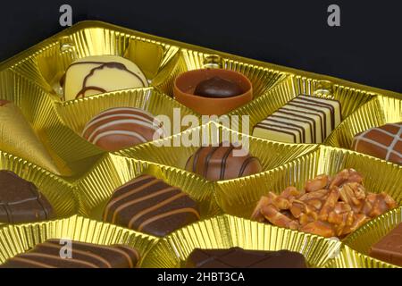 Praline di cioccolato diverse in una scatola d'oro. Primo piano di scatola di cioccolatini. Scatola di praline belghe di forme diverse Foto Stock
