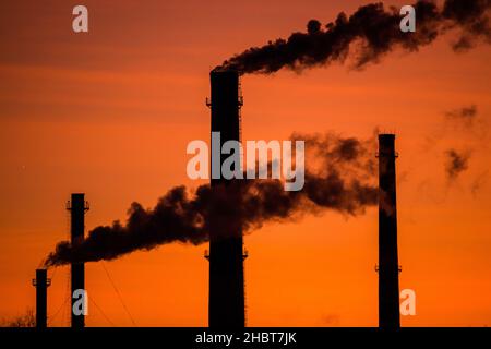 Silhouette di camini fumanti su sfondo di tramonto arancione Foto Stock