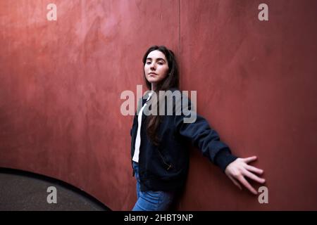 Adolescente donna appoggiata contro un muro colorato Rust Foto Stock