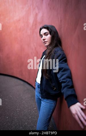 Adolescente donna appoggiata contro un muro colorato Rust Foto Stock