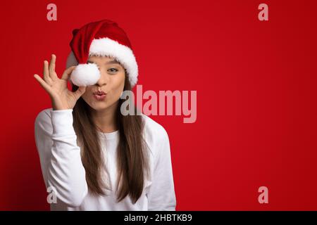 Buone feste. Giocosa giovane donna che indossa l'occhio di copertura di Santa Hat con Pompom Foto Stock