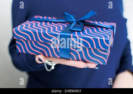Le mani femminili con le unghie lunghe tengono una scatola del regalo nei colori blu Foto Stock