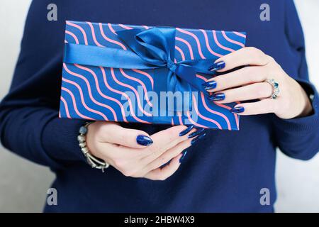 Le mani femminili con le unghie lunghe tengono una scatola del regalo nei colori blu Foto Stock