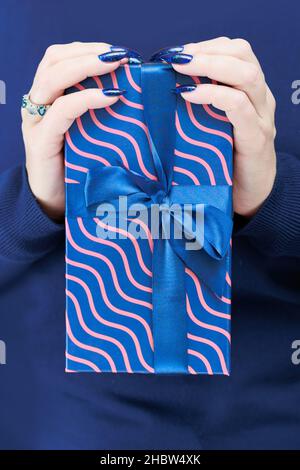Le mani femminili con le unghie lunghe tengono una scatola del regalo nei colori blu Foto Stock