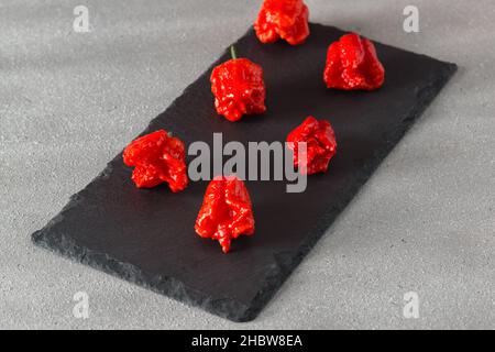 Sei cialde del pepe più caldo del mondo della varietà California Reaper giacciono su una pietra nera. Messa a fuoco selettiva Foto Stock