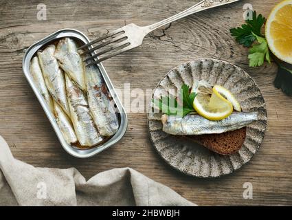 le sardine aperte possono forarsi e fette di pane su vecchio tavolo da cucina in legno Foto Stock