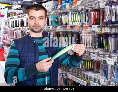 L'uomo cliente scegliendo le esche artificiali vicino a riposare nel negozio di articoli sportivi Foto Stock