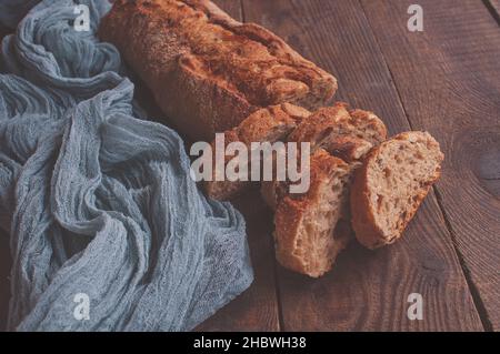 Pane fatto in casa cotto su un tavolo di legno con tovaglia di garza grigia, baguette fresche affettate su sfondo di legno Foto Stock