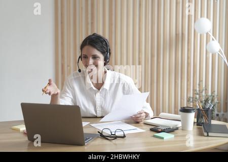 Happy tutor italiano in cuffia conduce il webinar online su un notebook in un moderno ufficio domestico Foto Stock