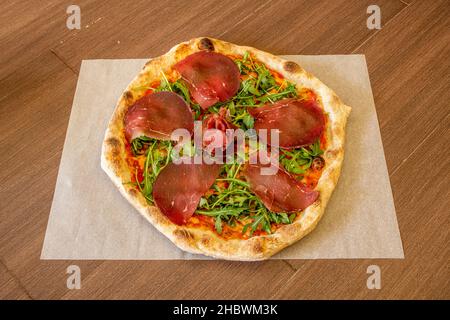 Pizza tirolese con carpaccio, rucola, pomodoro e crosta sottile con bordi tostati Foto Stock