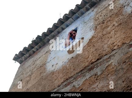 Una donna marocchina locale che guarda fuori attraverso una piccola finestra nella sua casa nella medina di Chefchaouen, Marocco. Foto Stock