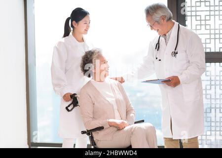 Medico a parlare con una donna anziana in una sedia a rotelle Foto Stock