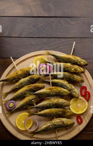 Sgombro di cavallo fritto, pesce istavrit bastoni di legno spiediti, sul piatto di legno. Vista dall'alto Foto Stock