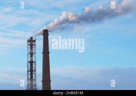 Due tubi industriali fumosi contro il cielo blu Foto Stock