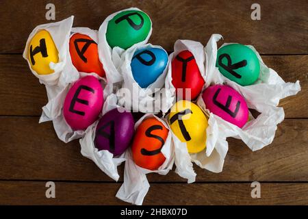 Uova di Pasqua colorate con le carte bianche sul tavolo di legno.scrittura a mano lettere di Pasqua felice sulle uova. Foto Stock