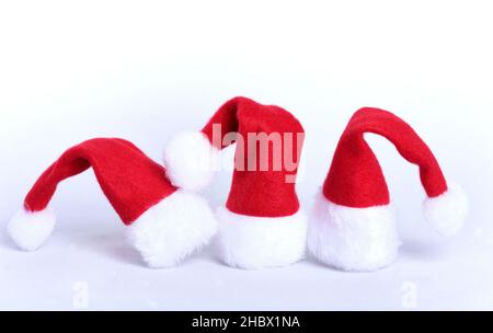 Tre cappelli rossi di Babbo Natale con un bordo bianco e un bobble bianco si ergono l'uno accanto all'altro di fronte ad uno sfondo bianco e sono tagliati, con spazio Foto Stock