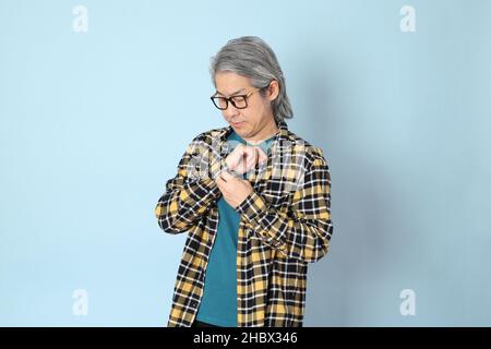 L'uomo asiatico senior con camicia a quadri gialla in piedi su sfondo blu. Foto Stock