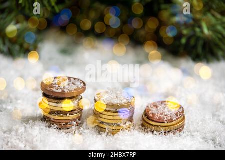 Piramidi d'oro di monete ricoperte di neve su sfondo di rami di abete rosso verde con bokeh da una ghirlanda. Concetto di ricchezza nel nuovo anno Foto Stock