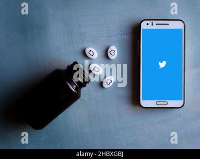 Concetto di dipendenza dai social media. Twitter logo sul telefono e mi piace, retweet icona su capsule bianche pillole Foto Stock