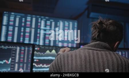 Uomo con barba lunga e capelli lunghi che fa l'analisi per il commercio di giorno su schermi di analisi di criptovaluta Foto Stock