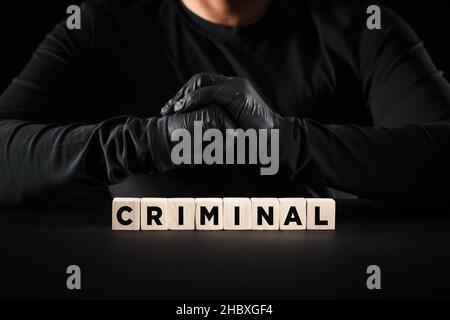 Concetto di criminalità, criminalità, ladro o furto. La parola criminale su blocchi di legno con un background di persona criminale. Foto Stock