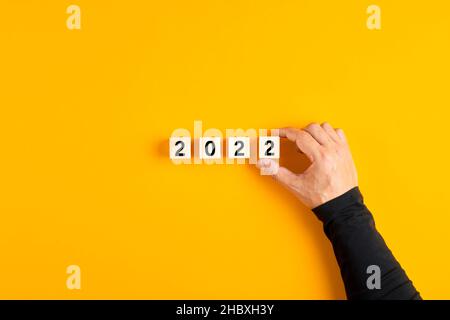 Mano maschio mettendo un cubo di legno con numero uno e completando l'anno 2022. progetto di pianificazione del nuovo anno 2022 o di obiettivi aziendali. Foto Stock