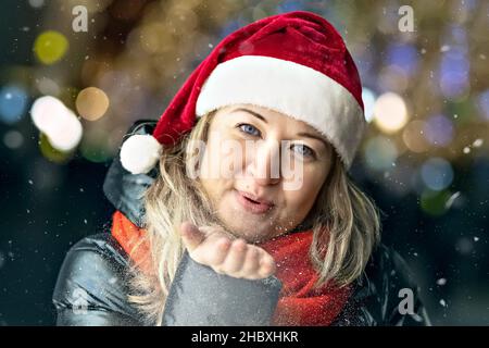 Shopping natalizio di una giovane donna. Sacchetti di carta colorati e luminosi con regali. Soffia i fiocchi di neve dalla mano. Foto Stock