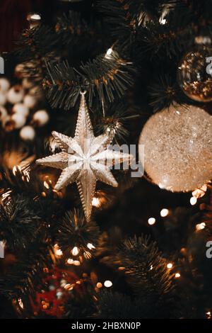 Rami verdi dell'albero di Natale decorati con ornamento stella scintillante d'argento e luce festosa delle ghirlande dorate. Stagione invernale di nuovo anno. Arredamento interno Foto Stock