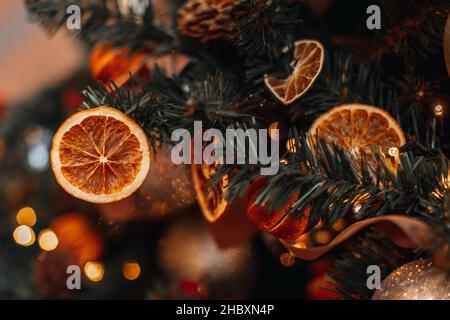 Rami di albero di Natale decorati con arance e mandarini secchi luminosi. Dettagli creativi e accoglienti e luci dorate delle ghirlande in bokeh sullo sfondo. Vinello Foto Stock